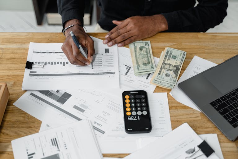 Man trying to avoid financial stress working with calculator, money, and laptop on a desk.
