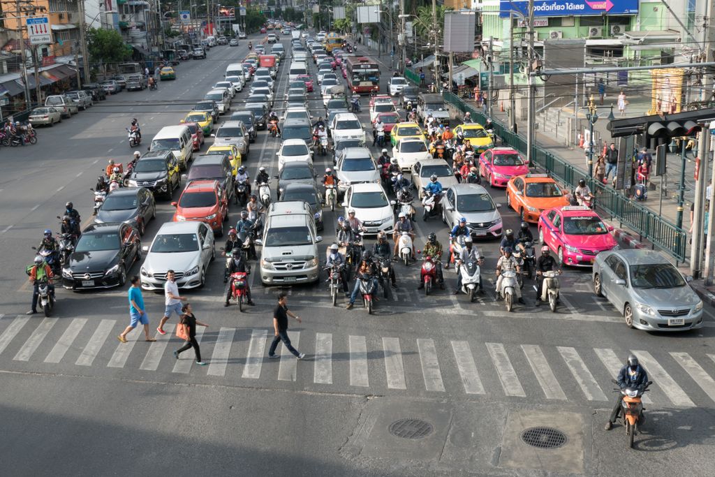 Aerial view of city traffic with cars and motorcycles at a busy intersection, including pedestrians crossing.